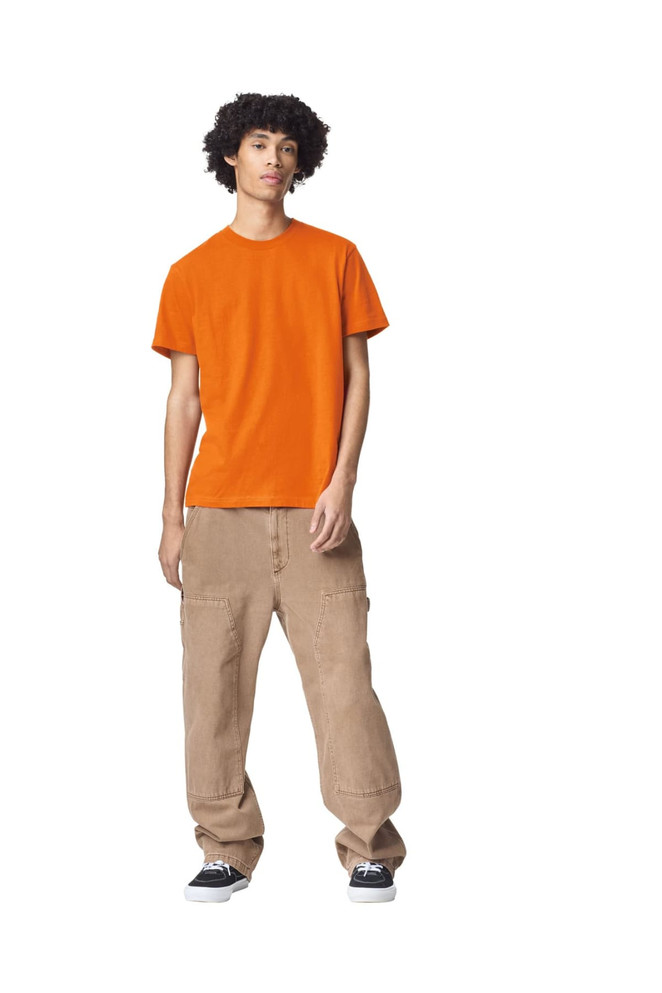An orange unisex short sleeve t-shirt worn by a model, paired with beige cargo pants. The t-shirt features a logo.