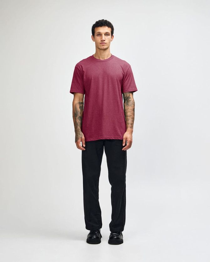 A model wearing a maroon unisex CVC short sleeve t-shirt paired with black trousers and shoes.