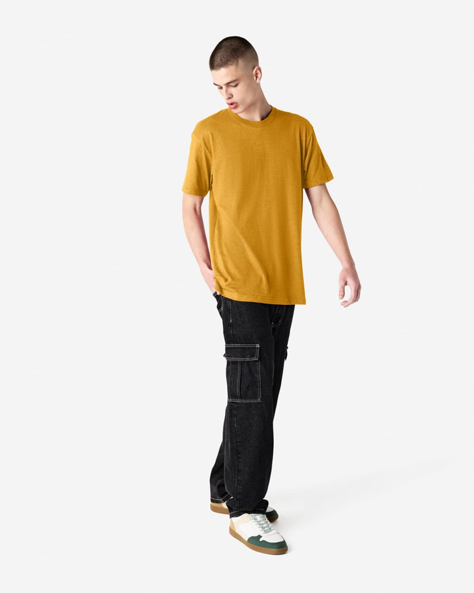A unisex short sleeve t-shirt in mustard yellow, worn with black cargo pants, featuring a logo.
