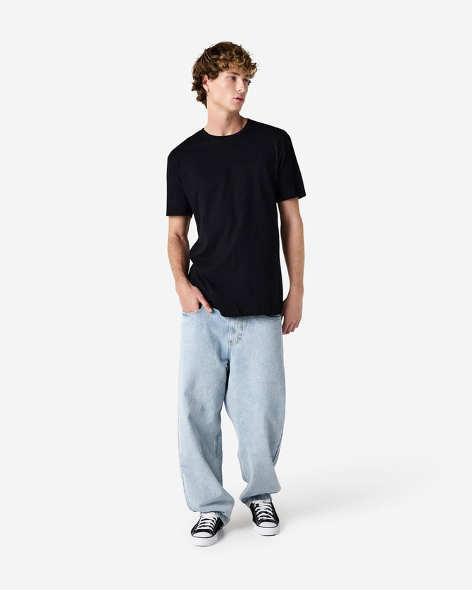 A black unisex short sleeve t-shirt worn with light blue baggy jeans and black sneakers. The model poses against a plain background.