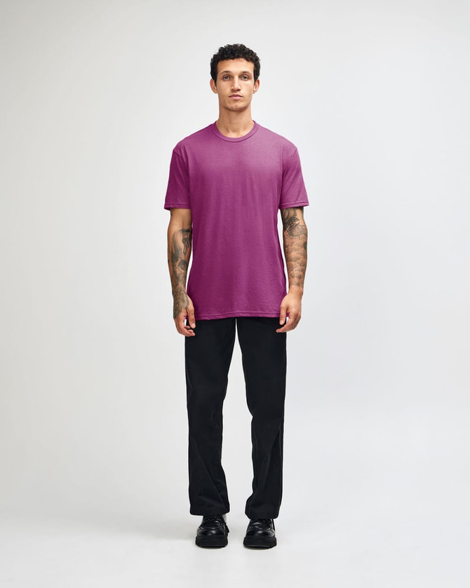 A unisex short sleeve T-shirt in vibrant pink, paired with relaxed black pants and a casual stance.