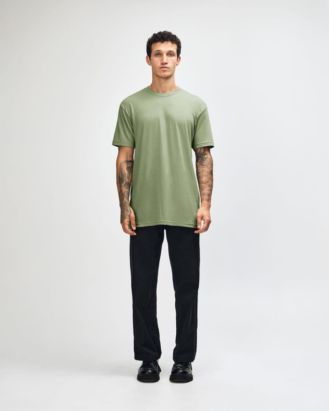 A model wearing a green unisex short sleeve T-shirt and black cargo pants, standing in a neutral setting.