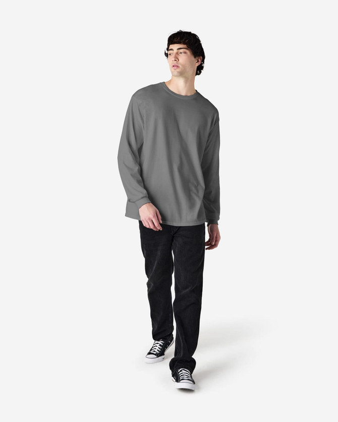 A long-sleeve T-shirt in grey worn by a model, paired with black jeans and sneakers. The shirt features a logo.