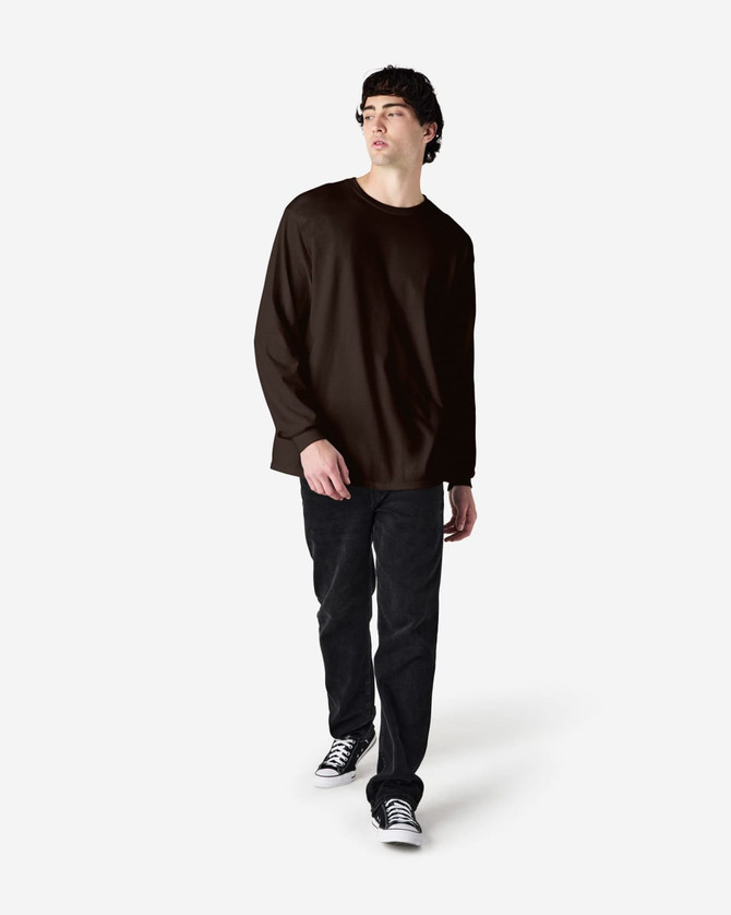A man wearing a brown long sleeve T-shirt and black jeans, standing against a plain background.