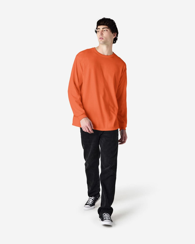 An orange long sleeve t-shirt worn by a standing male model, paired with black pants and sneakers.
