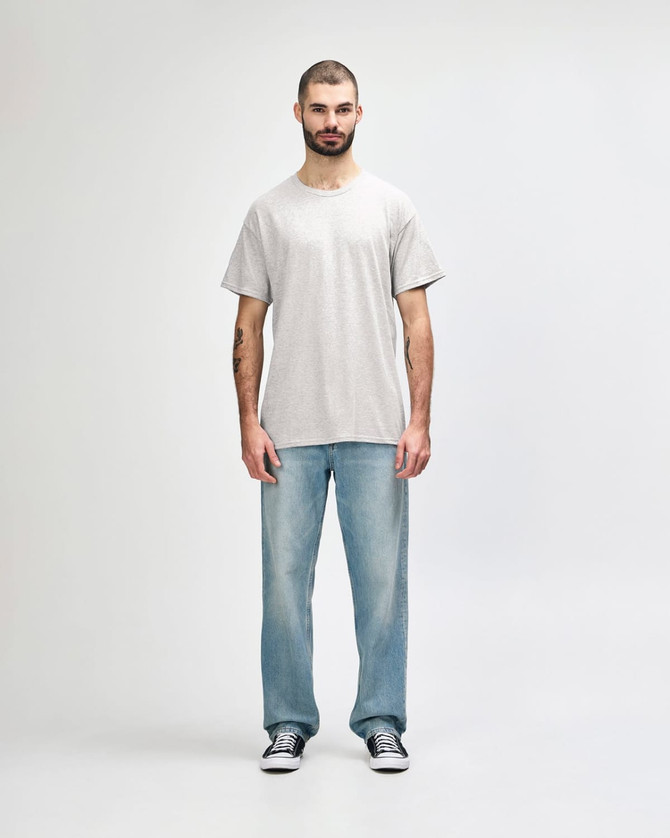 A grey Gildan Heavy Cotton adult T-shirt displayed on a person, paired with light blue jeans and black shoes.