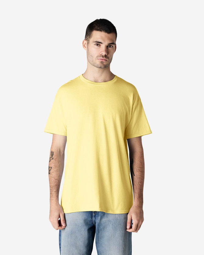 A model wearing a yellow Gildan Heavy Cotton adult T-shirt, paired with blue jeans. The shirt has a logo.