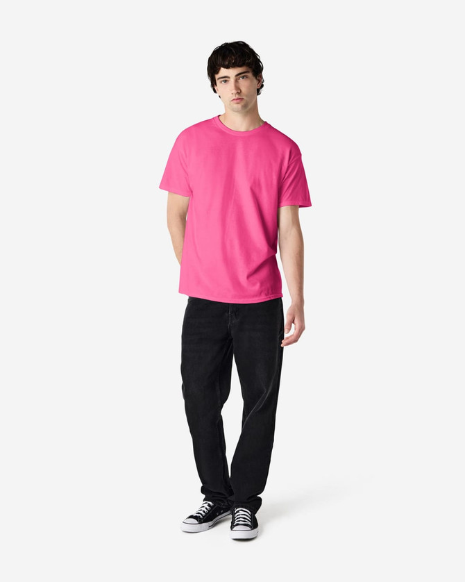 A model wearing a bright pink Gildan Heavy Cotton adult T-shirt paired with black pants and sneakers.