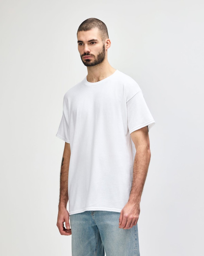 A white Gildan Heavy Cotton adult T-shirt displayed on a model with dark jeans. The shirt features a logo.