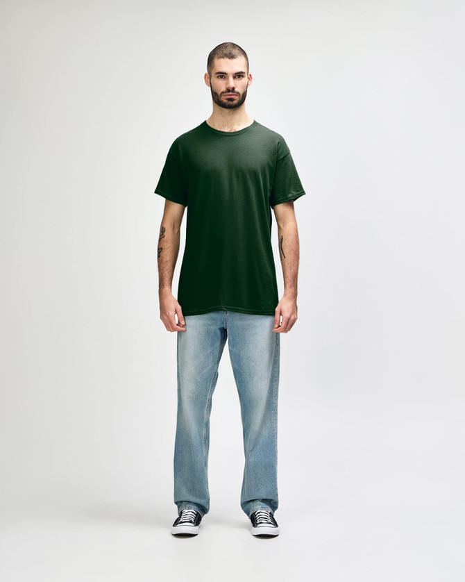 A green Gildan Heavy Cotton adult T-shirt displayed on a male model, paired with black jeans and sneakers.