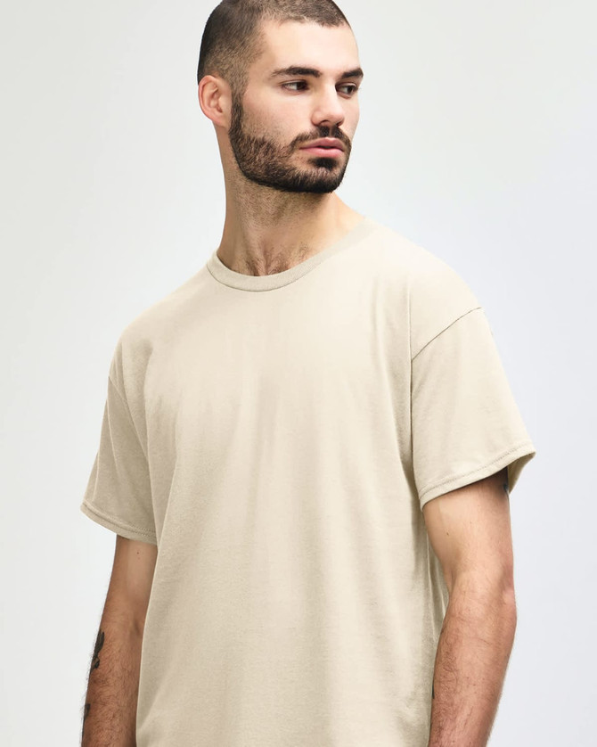 A beige Gildan Heavy Cotton Adult T-Shirt on a model, featuring a round neckline and a logo.