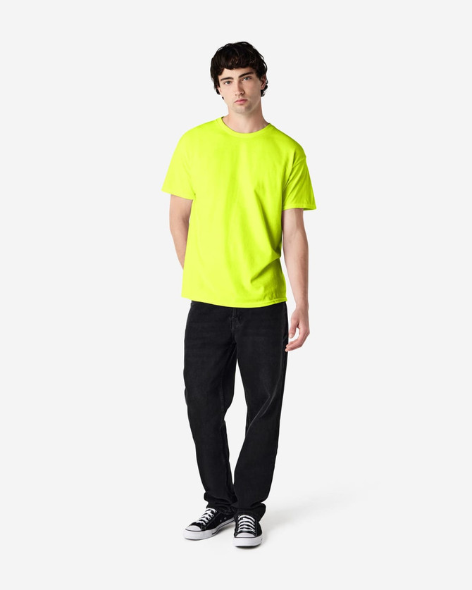 A man stands wearing a bright yellow Gildan Heavy Cotton Adult T-Shirt and black jeans, with sneakers.