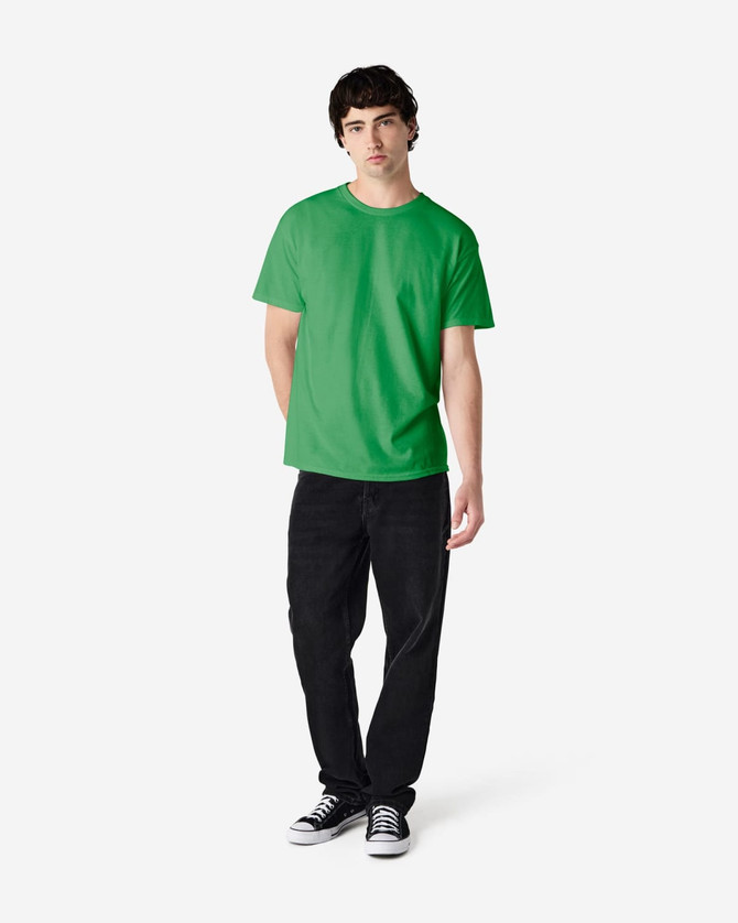 A green Gildan Heavy Cotton adult t-shirt displayed on a model wearing black jeans and sneakers, with a logo present.