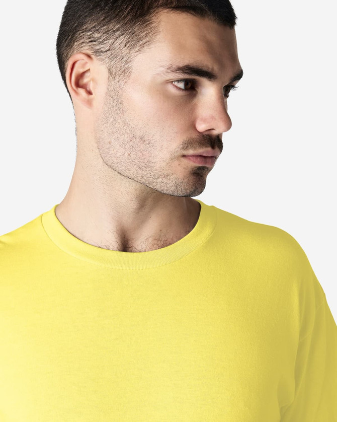 A close-up of a man wearing a bright yellow Gildan Heavy Cotton Adult T-Shirt. The shirt has a logo on it.