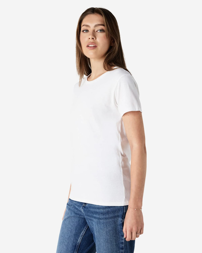 A white Gildan Heavy Cotton Ladies' T-Shirt displayed on a model, paired with blue jeans. The shirt has a simple design and a logo.