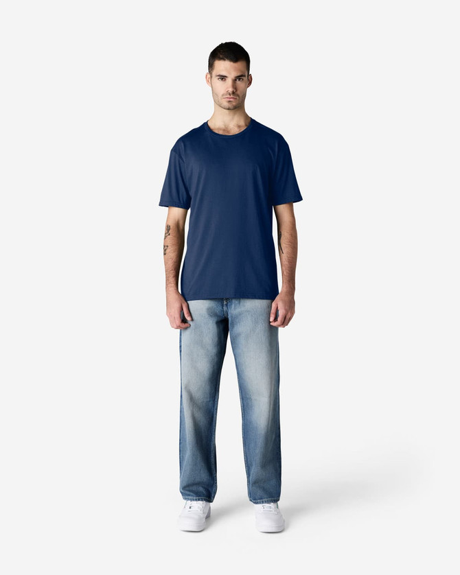 A navy Gildan Softstyle adult T-shirt displayed on a male model, paired with light blue jeans and white shoes.