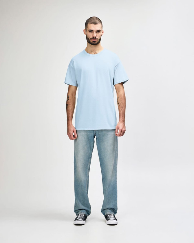 A plain light blue Gildan Softstyle adult T-shirt worn with straight-leg jeans and white shoes, featuring a logo.