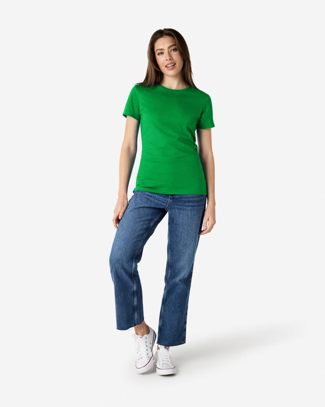 A green Gildan Softstyle ladies' t-shirt paired with blue jeans and white sneakers, modelled by a woman.