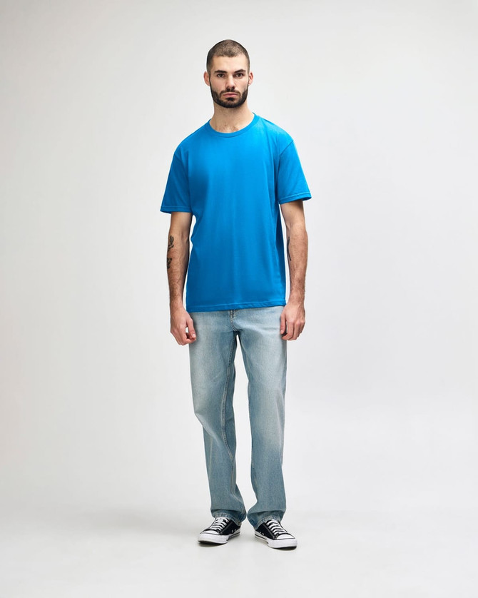 A man wearing a bright blue Gildan Softstyle adult midweight T-shirt and black jeans, with a casual stance.