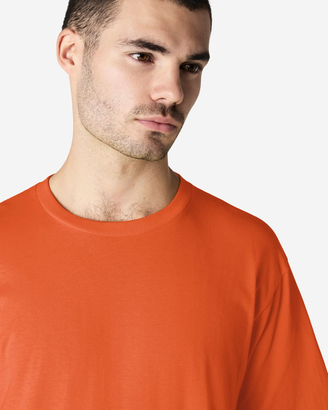 An orange Gildan Softstyle adult midweight t-shirt worn by a model. The shirt has a round neckline and short sleeves.