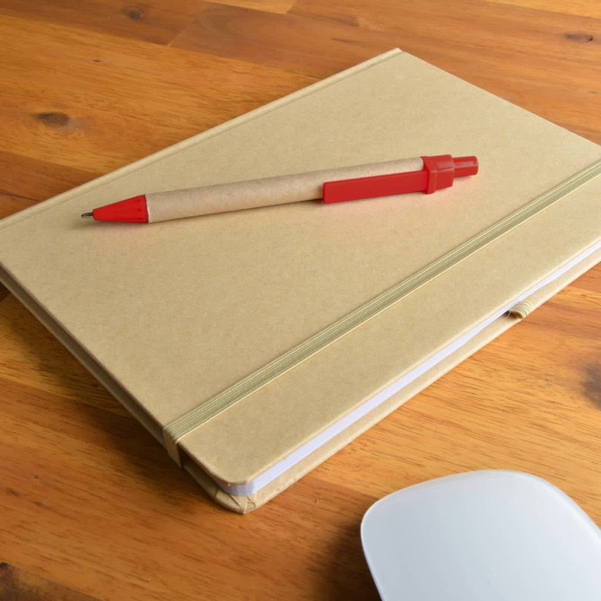 A Natura A5 notebook with a kraft cover and a Matador pen resting on top, placed on a wooden surface.