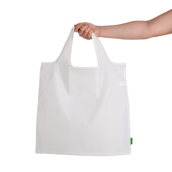 A white reusable grocery bag is held by a hand, featuring a logo on the side.