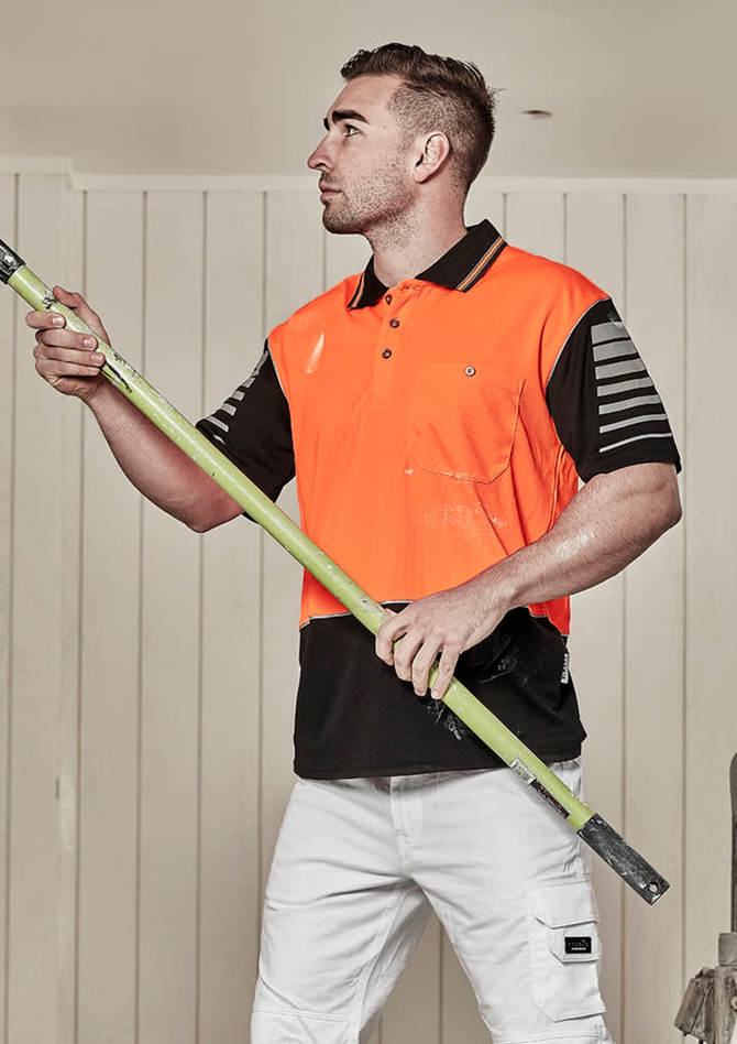 A man wearing an orange and black short sleeve polo shirt stands holding a green pole. The shirt has a logo.
