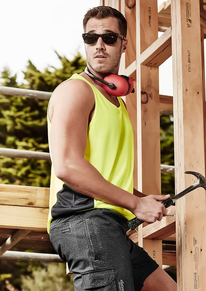 A man wearing a bright yellow hi-vis singlet and sunglasses, holding a hammer, with a construction backdrop.