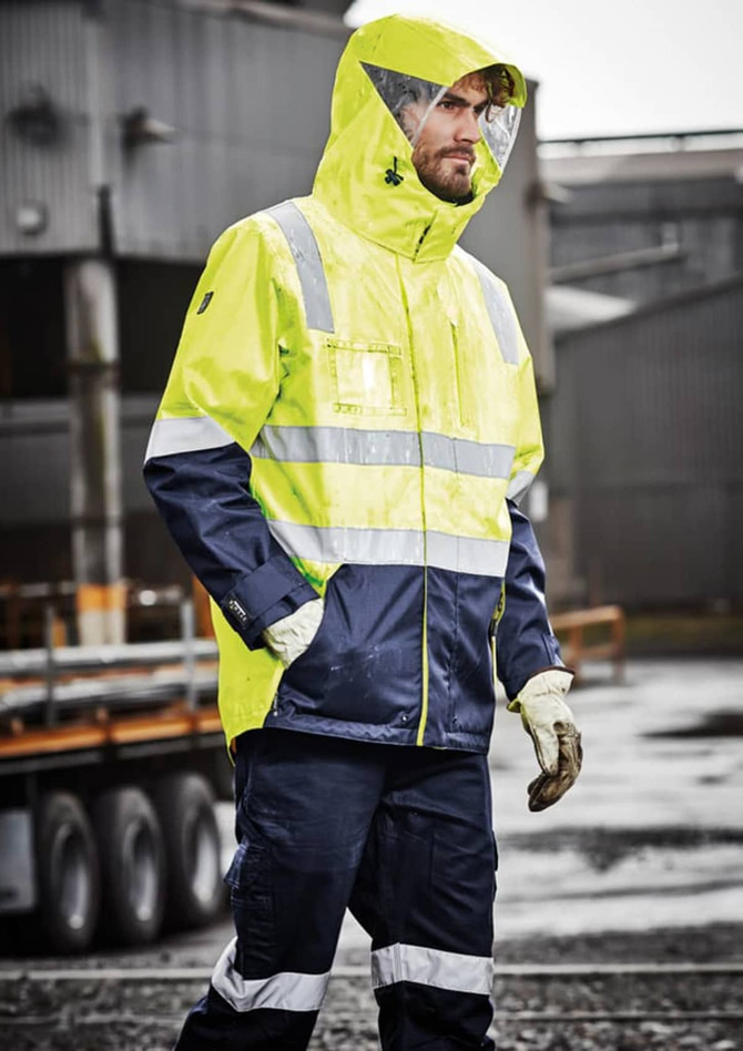 A hi-vis waterproof jacket in bright yellow and navy, featuring reflective strips and a hood. The model wears gloves.