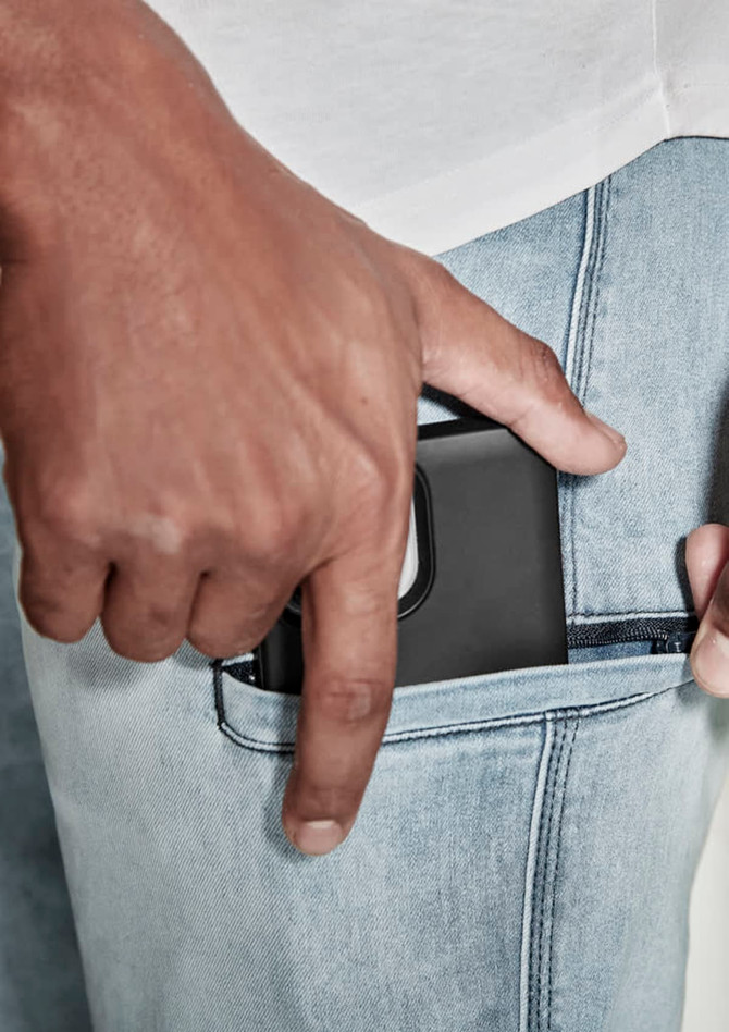 A close-up of a hand placing a phone into the pocket of light blue stretch jeans. The jeans feature a subtle logo.