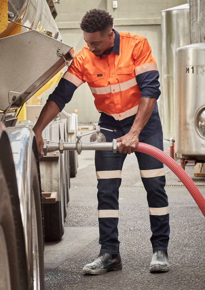 A worker in orange and navy bio motion taped stretch jeans operates equipment in a work environment, featuring reflective strips.