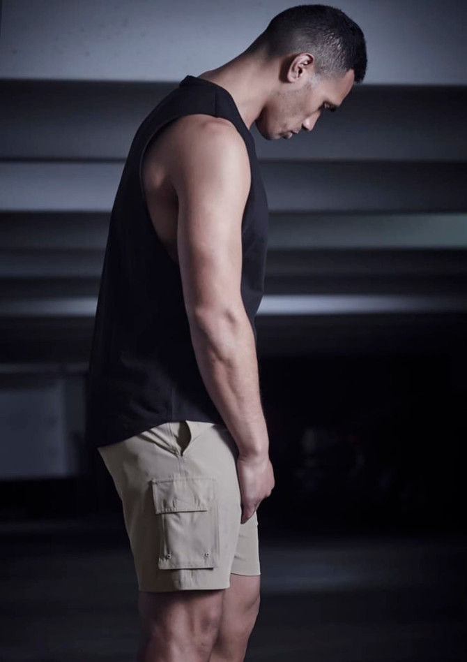 A man wearing khaki sports shorts and a black sleeveless top, standing in a dimly lit space.