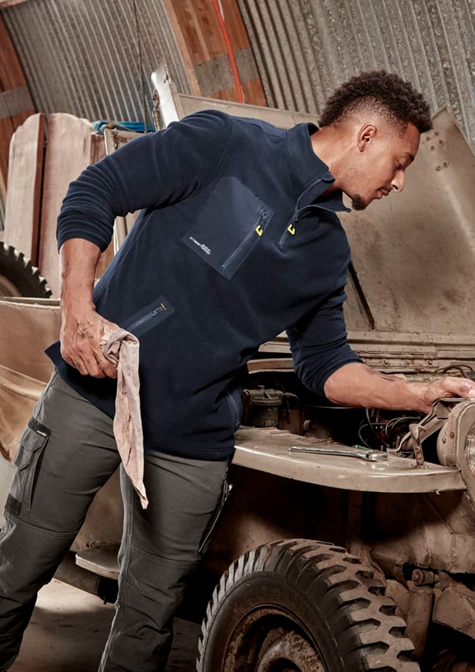 A man in a navy lightweight 1/4 zip polar fleece, working on a vehicle, with a logo on the garment.