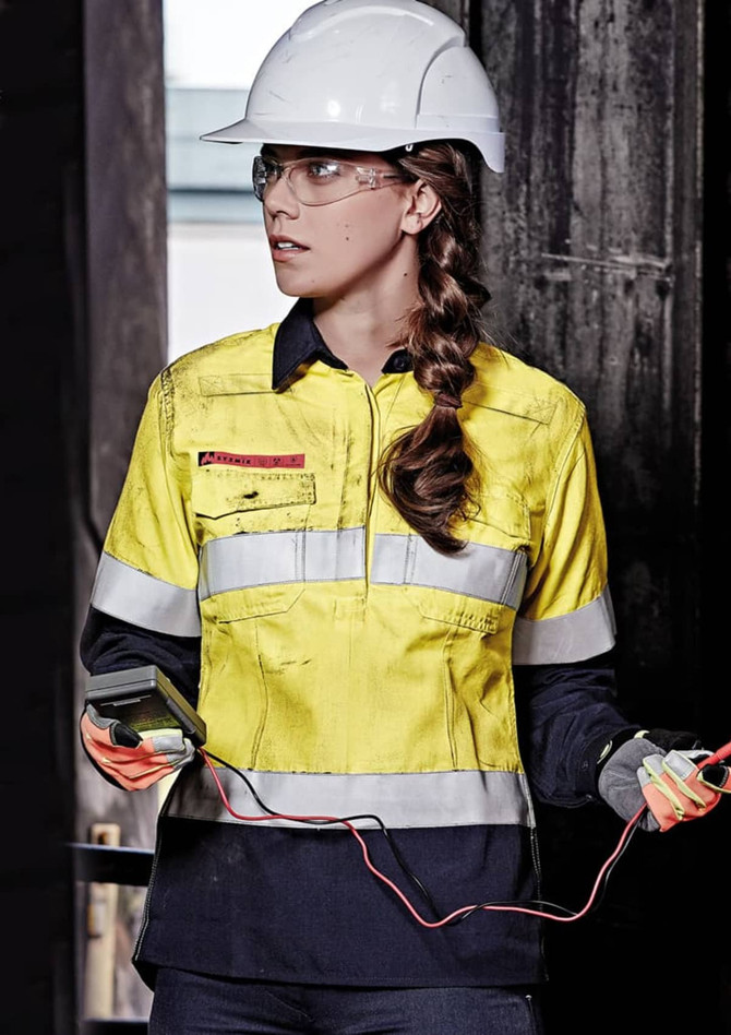 A yellow and navy women's safety shirt with reflective strips, worn with a hard hat and safety glasses.