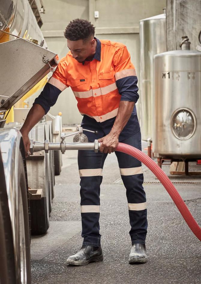 A man wearing an orange and navy long sleeve shirt with reflective tape, engaged in a work task outdoors.