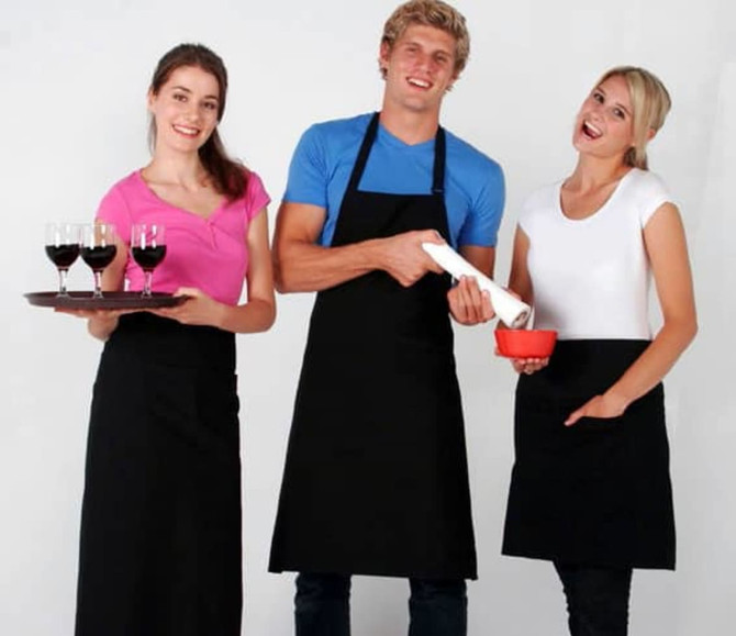 A full-bib apron in black is worn by a smiling man, flanked by two women holding drinks and a bowl.