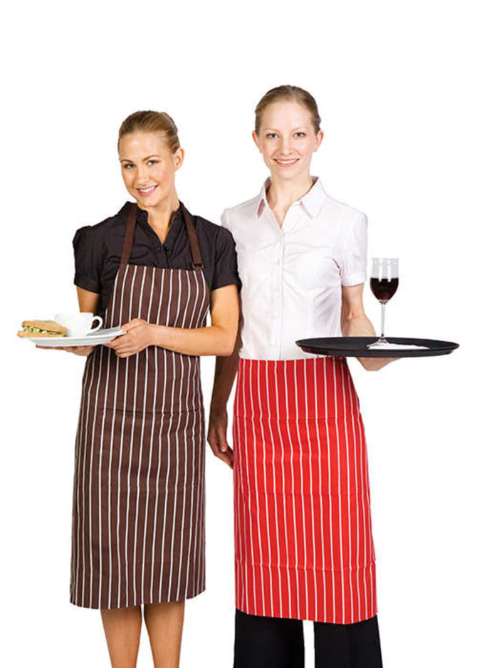 Two women are wearing striped full bib aprons, one in brown and the other in red, holding a plate and a tray.