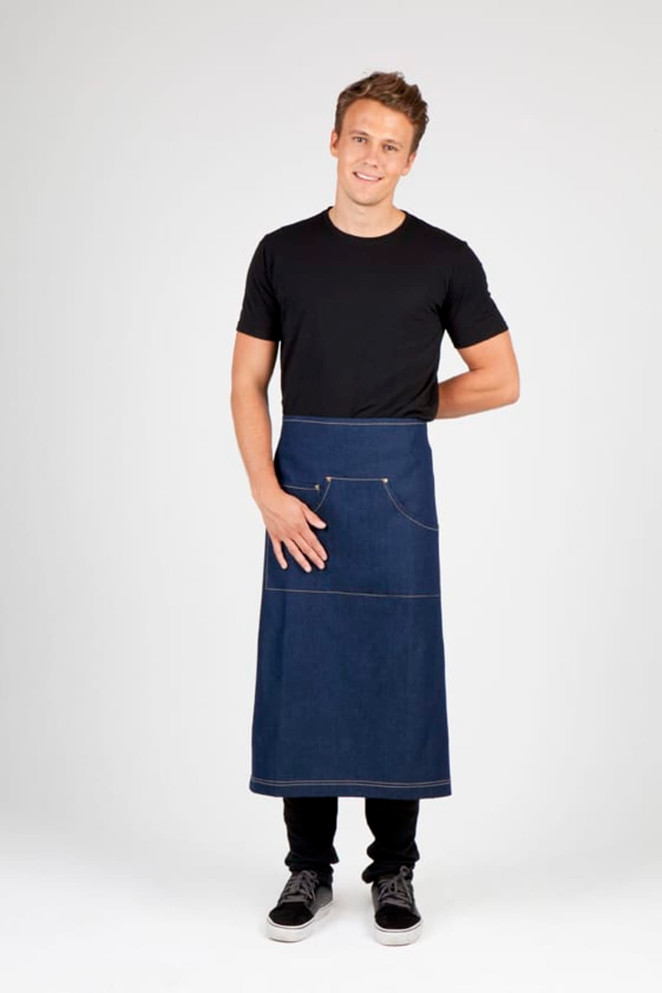 A man in a black t-shirt wears a long denim apron featuring a pocket and a logo.