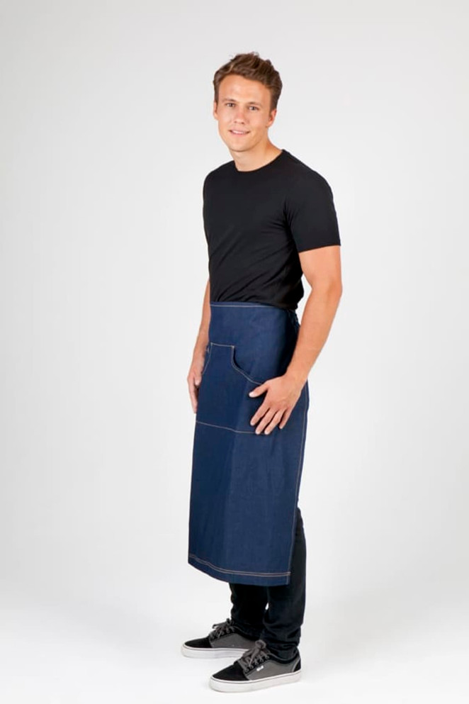 A man wearing a long denim apron with a pocket, standing against a neutral background. 
