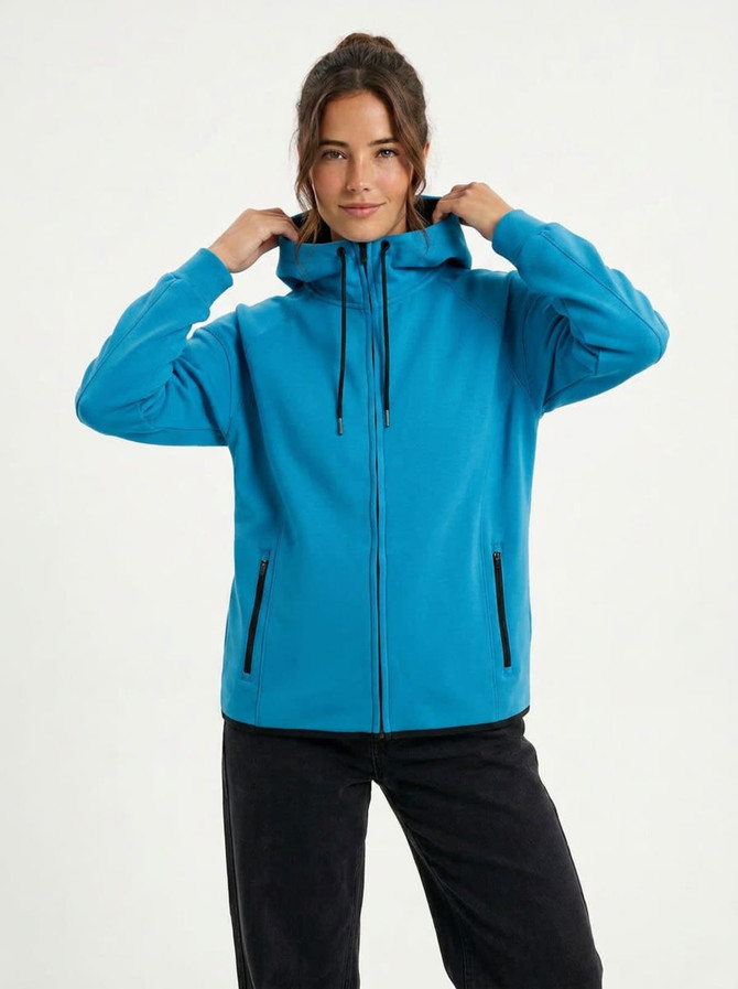 A woman wearing a blue soft cotton bonded polar fleece hoodie with a hood and zip front, featuring side pockets.