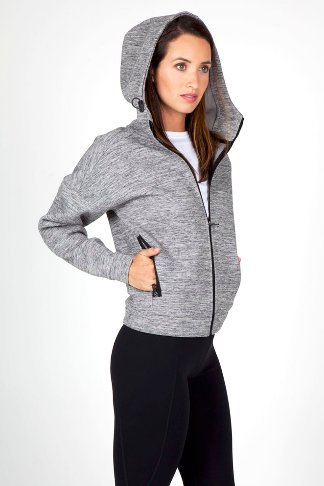 A grey women's hoodie featuring a zip front, large hood, and pockets, modelled by a woman.