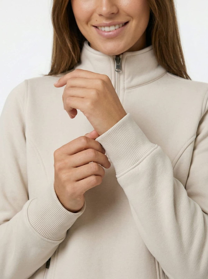 A beige women's half zip fleece jumper featuring a high collar and fitted cuffs, with a branding logo visible.