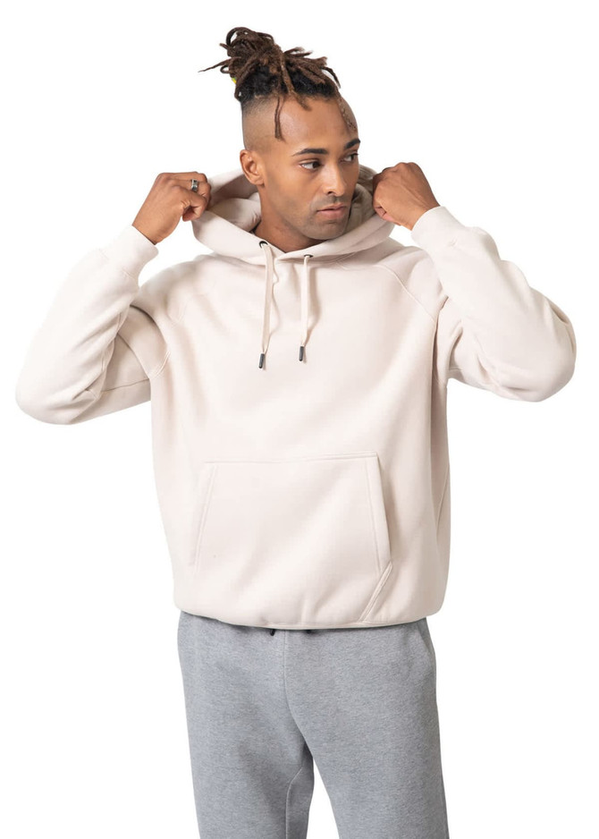 A light beige kangaroo hoodie featuring a front pocket, worn by a model with grey pants. The hoodie has a logo.