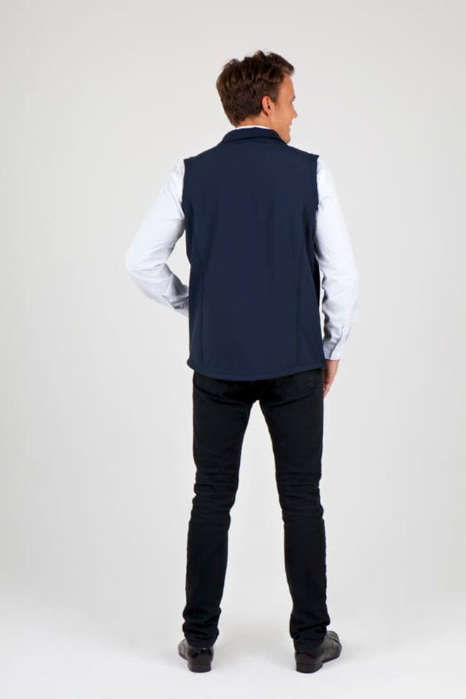 A man wearing a navy blue soft shell vest, seen from the back, paired with black pants. The vest has a logo.