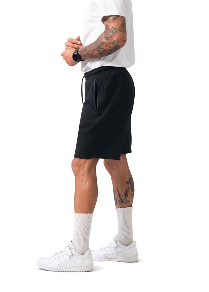 Men's black cotton sandwich shorts with an elastic waistband and pockets, modelled by a person wearing a white T-shirt and sneakers.