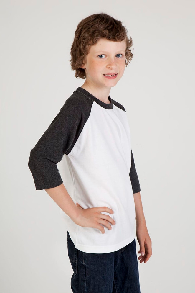 A child models a white and dark grey 3/4 raglan sleeve t-shirt with a logo on the front.