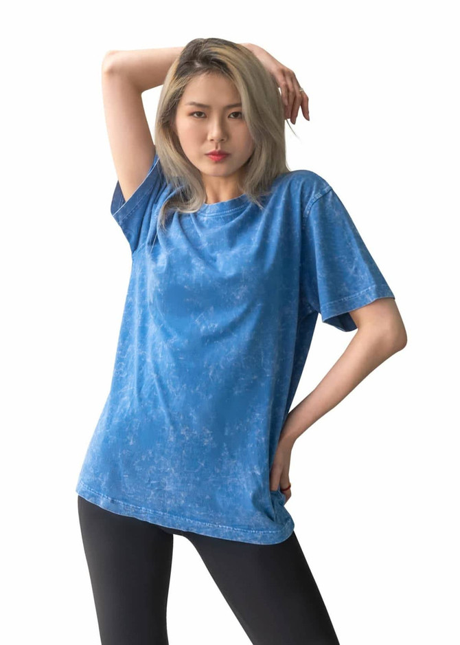 A unisex stone wash T-shirt in blue, featuring a relaxed fit and a logo. Modelled by a person with long, light hair.