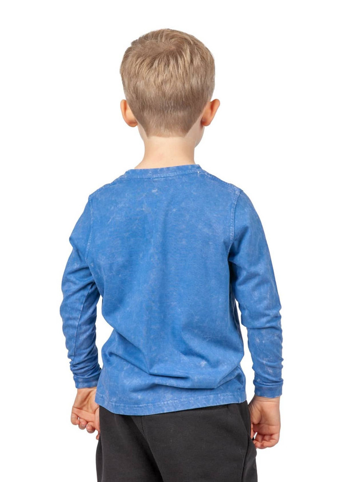 A boy wearing a blue stone wash long sleeve T-shirt, smiling and standing sideways against a white background.