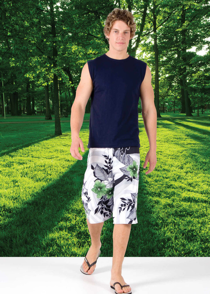 A man wearing a navy muscle T-shirt and floral shorts, standing on a grassy area with trees in the background.