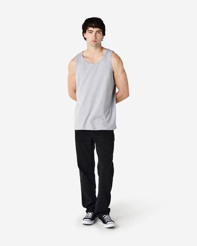 A grey Gildan Heavy Cotton adult tank top displayed on a model, paired with black pants and sneakers.